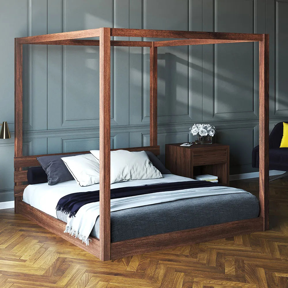 Wooden low four poster bed in a room with gray paneled walls and wooden flooring.